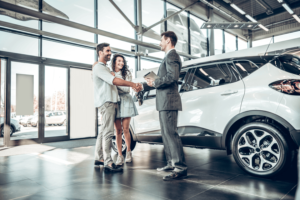 young couple shaking hands with auto salesman