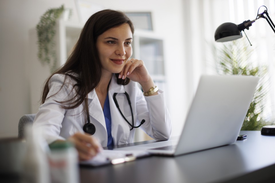 Smiling female doctor working on laptop in the office - stock photo
